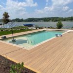 A large in-ground pool with a lake in the background.