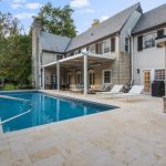 A large pool with chairs and a house in the background.