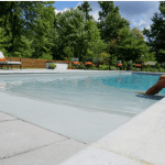 A woman in a hat sits on the edge of a pool.