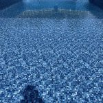 A pool with blue tiles and a person swimming in it.